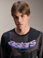 Alpinestars A-Dura Hollow Camo Jersey de manga larga, color camuflaje negro con gráfico 'astars' morado en el pecho, toma de estudio de un modelo masculino con ropa de MTB, estilo técnico y casual de bicicleta de montaña