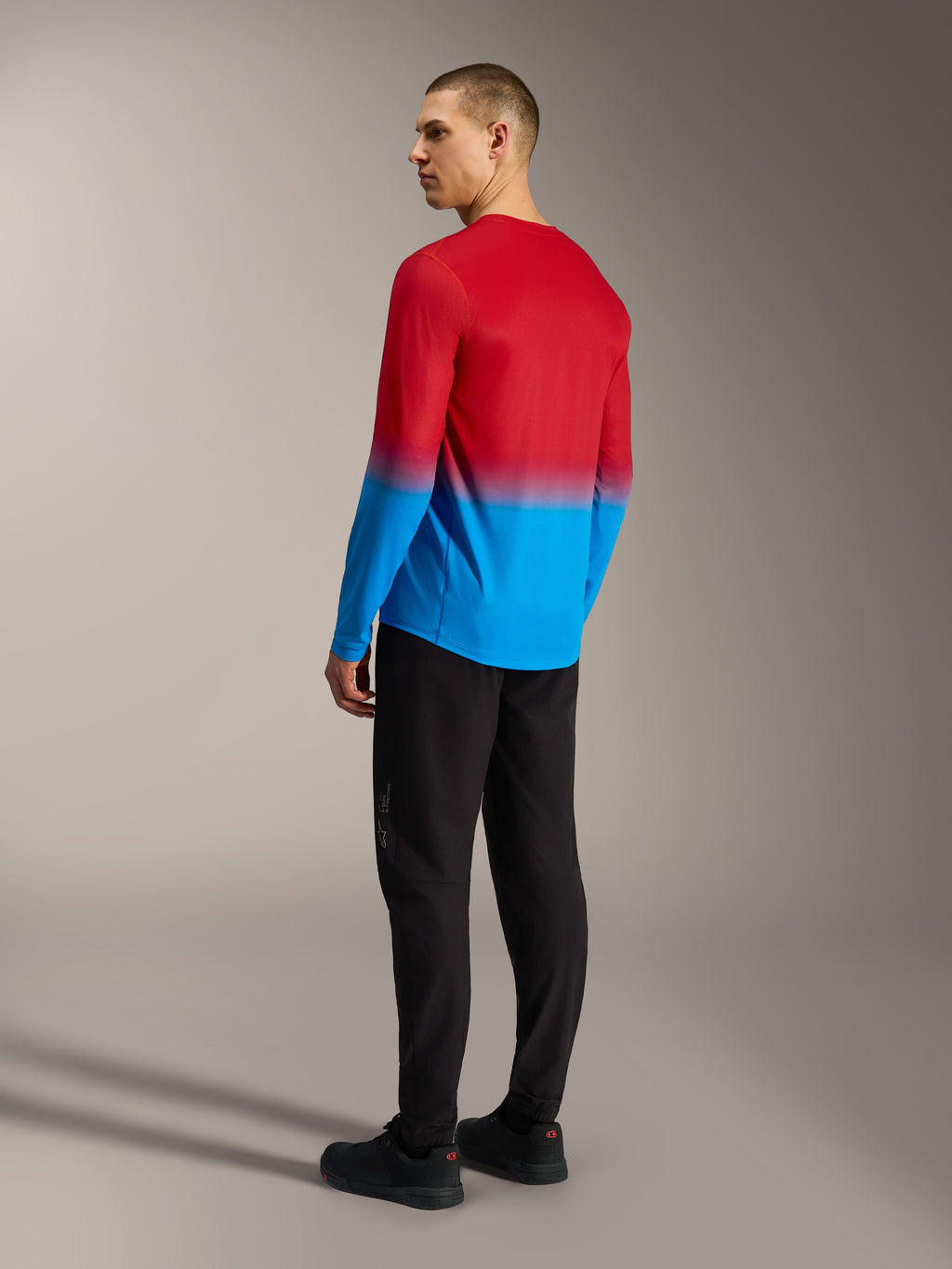 Camiseta MTB Alpinestars A-Dura ASTARS 2.0 manga larga, degradado rojo y azul, vista trasera sobre pantalones negros.