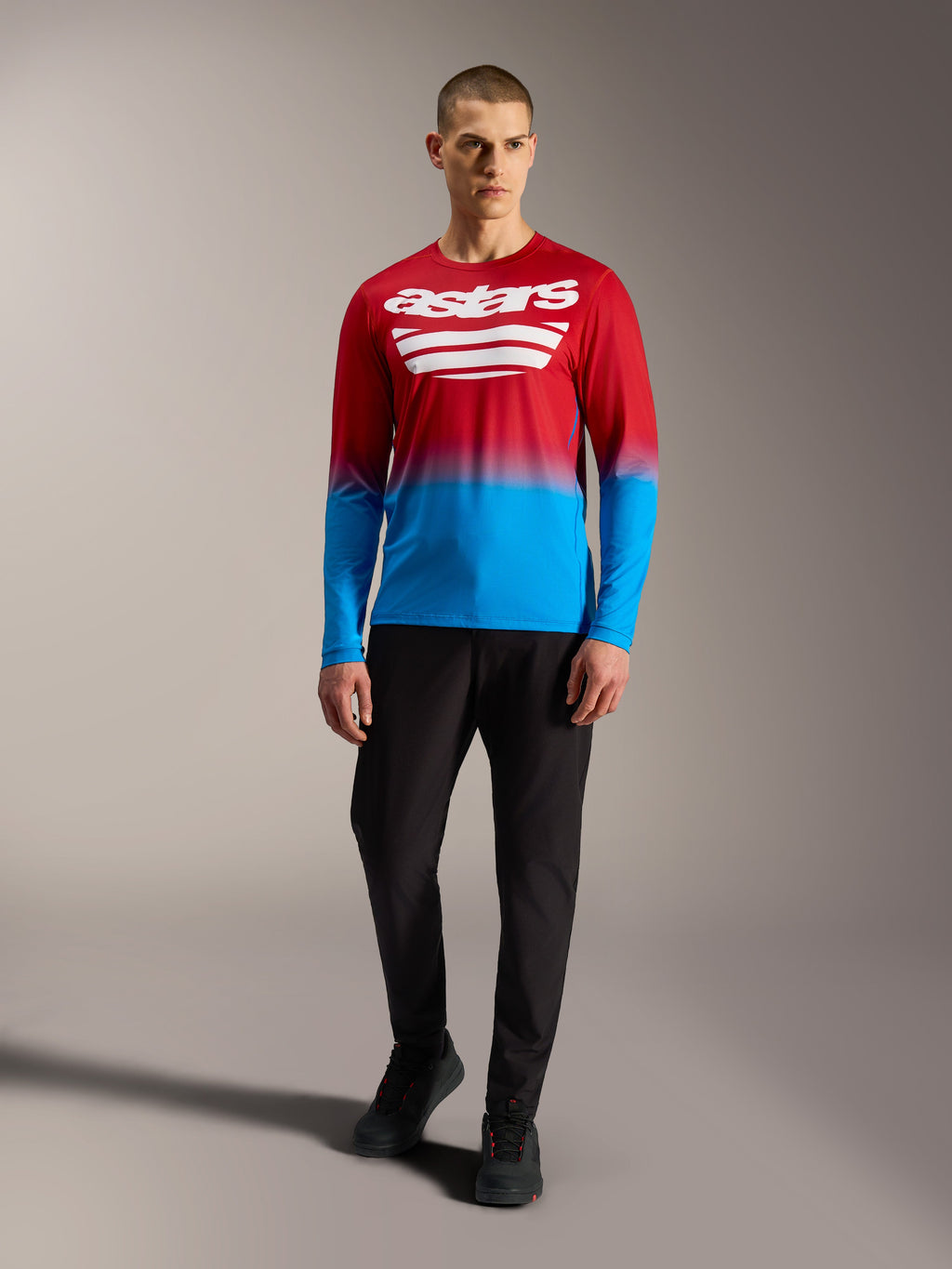 Camiseta MTB A-Dura ASTARS 2.0 de manga larga, degradado rojo y azul con logos blancos, combinada con pantalones negros.