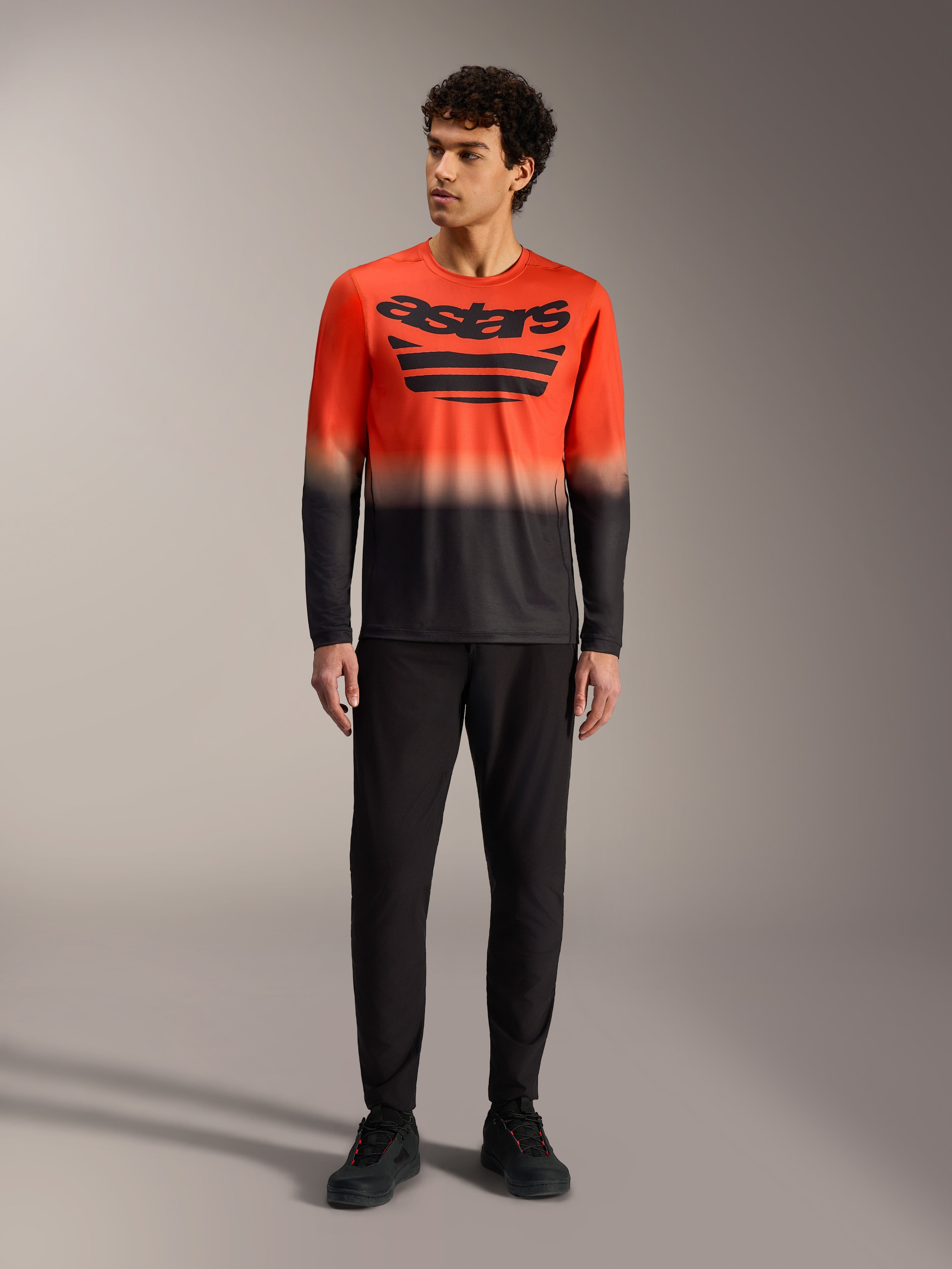 Camiseta A-Dura ASTARS 2.0 de manga larga, degradado naranja y negro con logo en el pecho y pantalones de MTB negros.