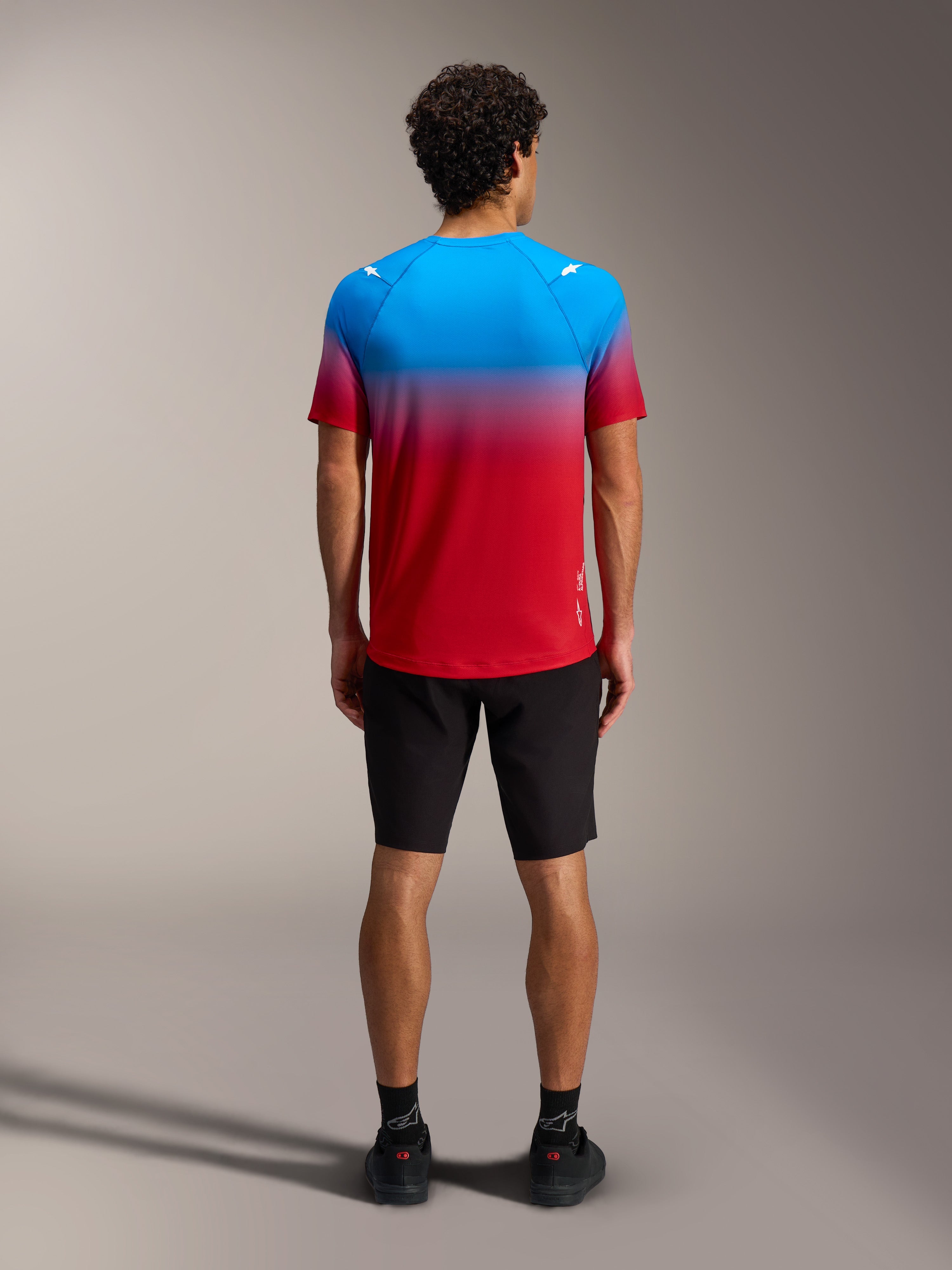 Maillot A-Dura ASTARS 2.0 de manga corta, degradado azul y rojo, vista trasera con shorts negros para ciclismo de montaña.
