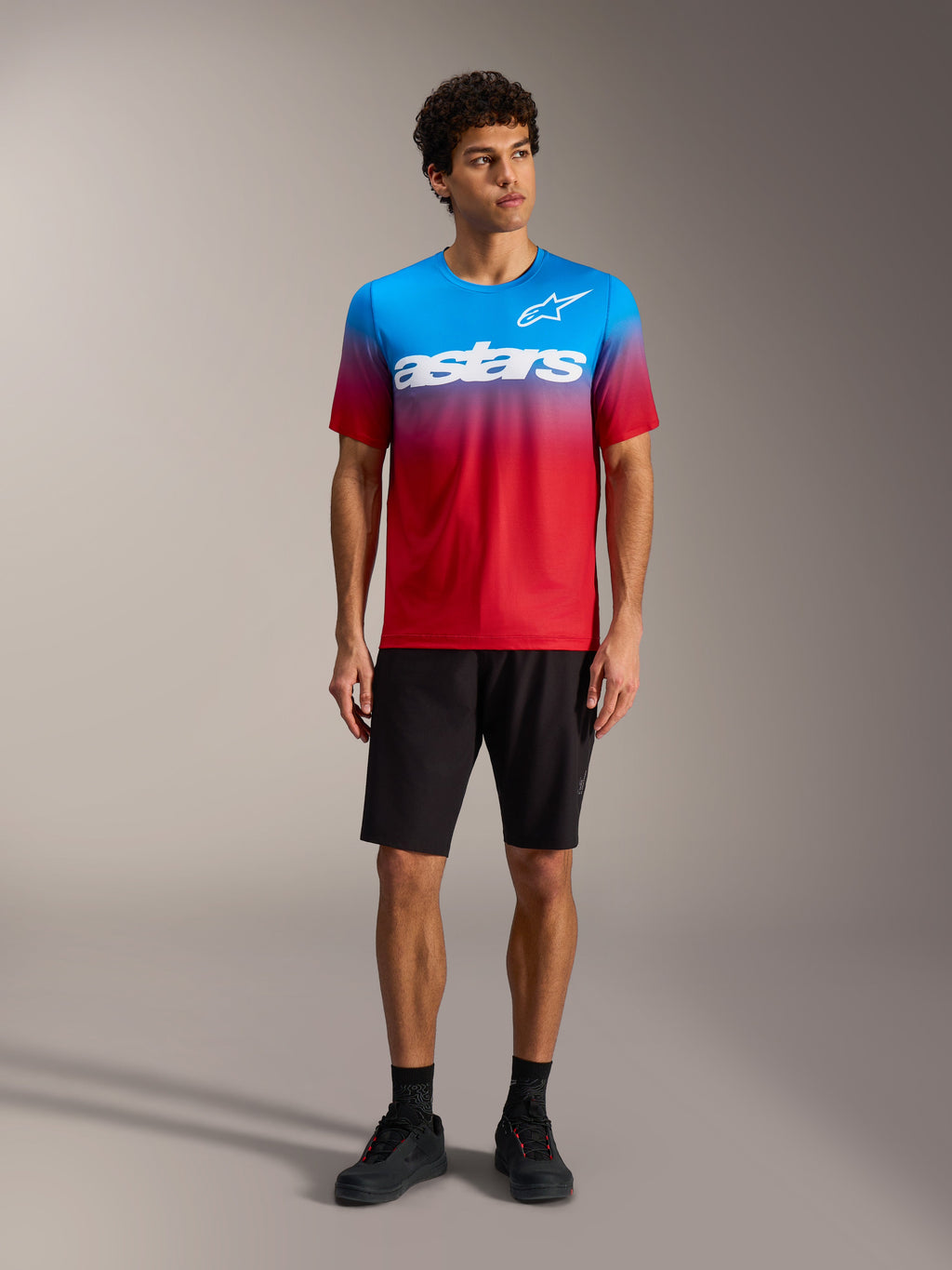 Maillot A-Dura ASTARS 2.0 en degradado rojo y azul con logo blanco, junto a shorts de MTB y calzado negros.