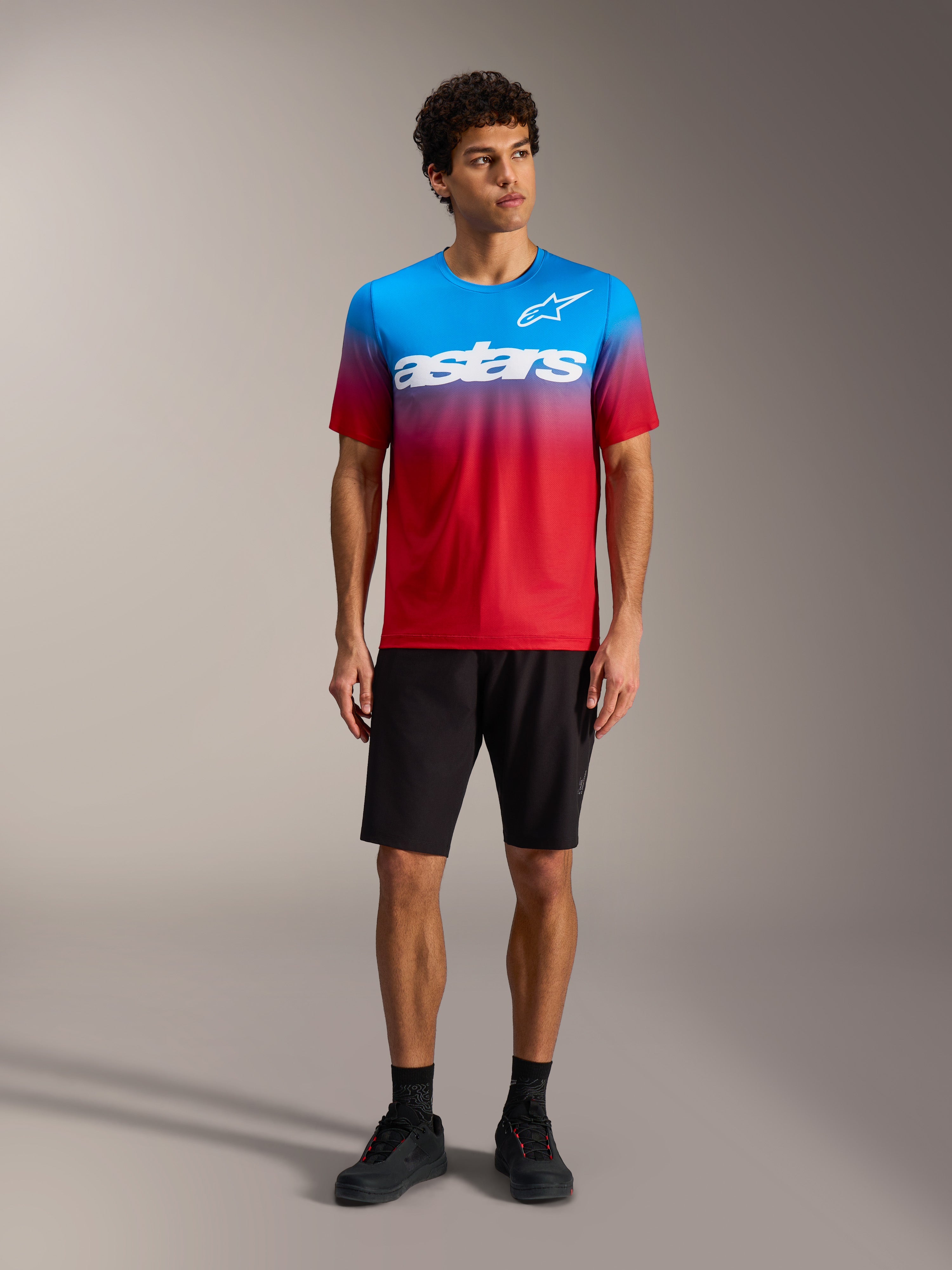 Maillot A-Dura ASTARS 2.0 en degradado rojo y azul con logo blanco, junto a shorts de MTB y calzado negros.