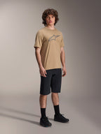 Jersey de manga corta Alpinestars A-Dura Astar, marrón claro, con un gran logotipo Astar gris oscuro en el pecho, lucido por un modelo con pantalones cortos de MTB negros, calcetines y zapatillas negras, ropa técnica casual para bicicleta de montaña en un entorno de estudio