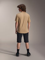 Modelo masculino de espaldas vistiendo los shorts Alpinestars A-Dura en color negro y un jersey de manga corta A-Dura en color tostado, combinado con calcetines negros y zapatillas de mountain bike, conjunto funcional para trail de MTB