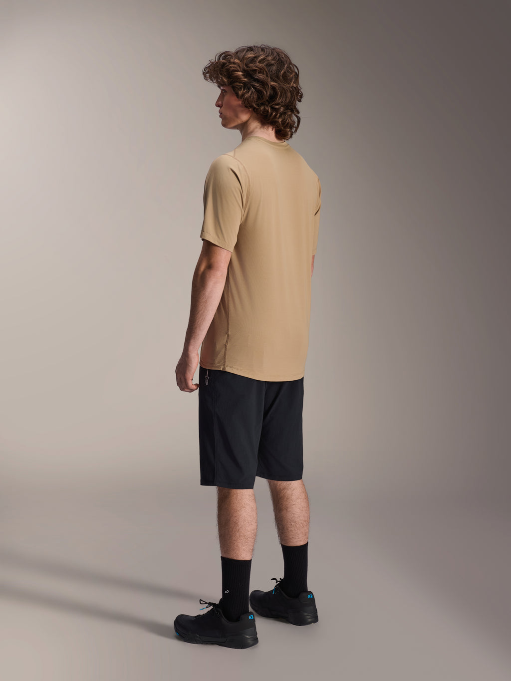 Shorts Alpinestars A-Dura Liner en negro y Jersey A-Dura SS en color arena, vistos de perfil en un modelo masculino, combinados con calcetines negros y zapatillas de ciclismo, ropa de estilo de vida de ciclismo de montaña.