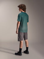 Alpinestars A-Dura Rise Jersey, jersey de MTB de manga corta, color verde Silver Pine, usado con pantalones cortos grises y zapatillas negras, vista trasera que muestra la cola más larga y el ajuste regular, tejido ligero que absorbe la humedad para ciclismo de montaña