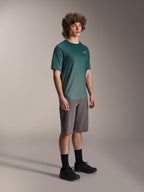 Alpinestars A-Dura Rise Jersey - Manga Corta en Silver Pine, jersey de ciclismo de montaña verde usado por un modelo con pantalones cortos grises y zapatillas negras, equipamiento casual para rutas de MTB con un pequeño logo blanco en el pecho