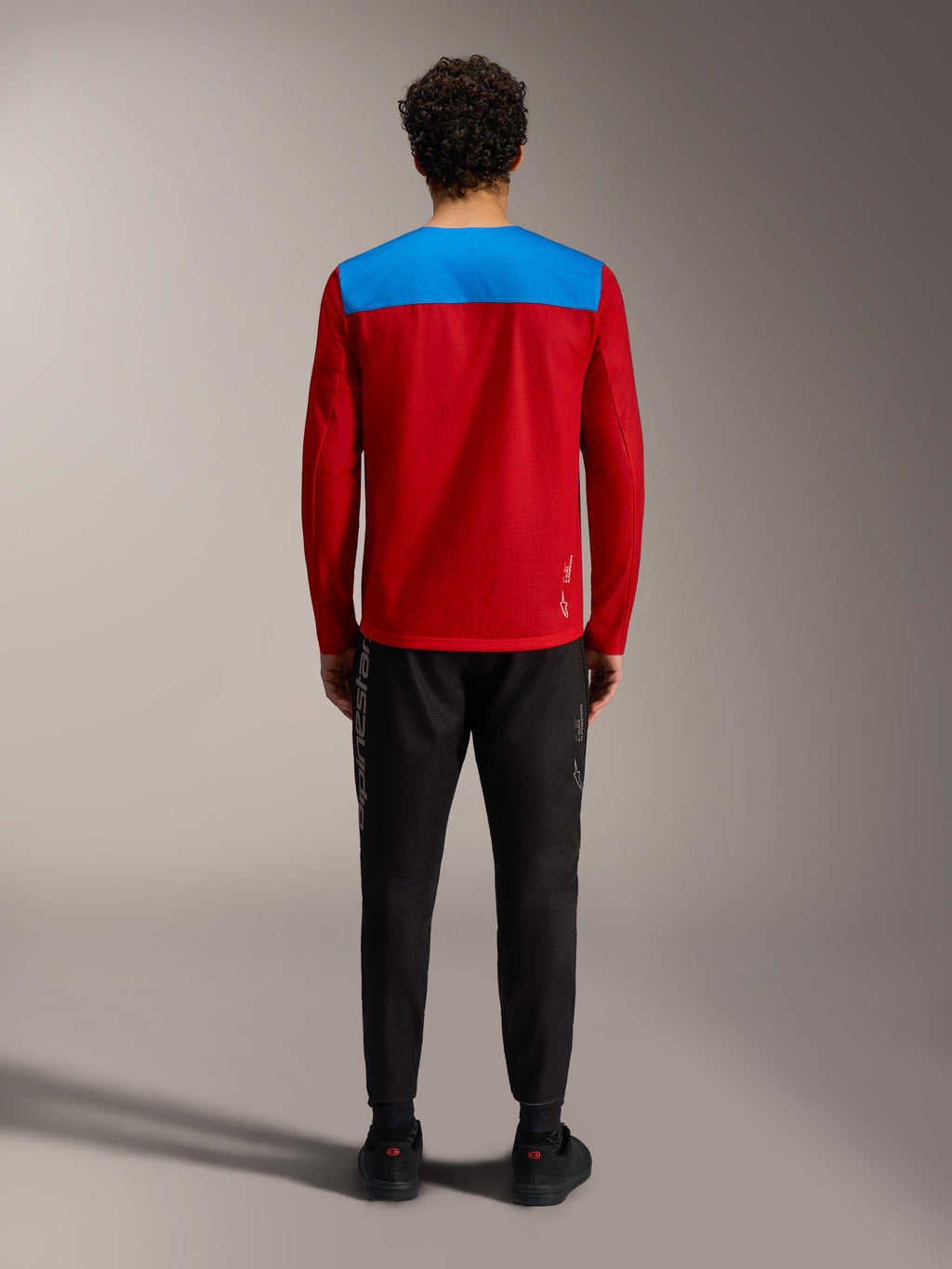 Jersey Alpinestars A-Dura Elite 2.0 de manga larga, modelo rojo y azul visto desde atrás con pantalones negros.