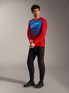 Jersey A-Dura Elite 2.0 rojo con panel de rayas azules en el pecho, logo blanco y pantalones MTB negros.