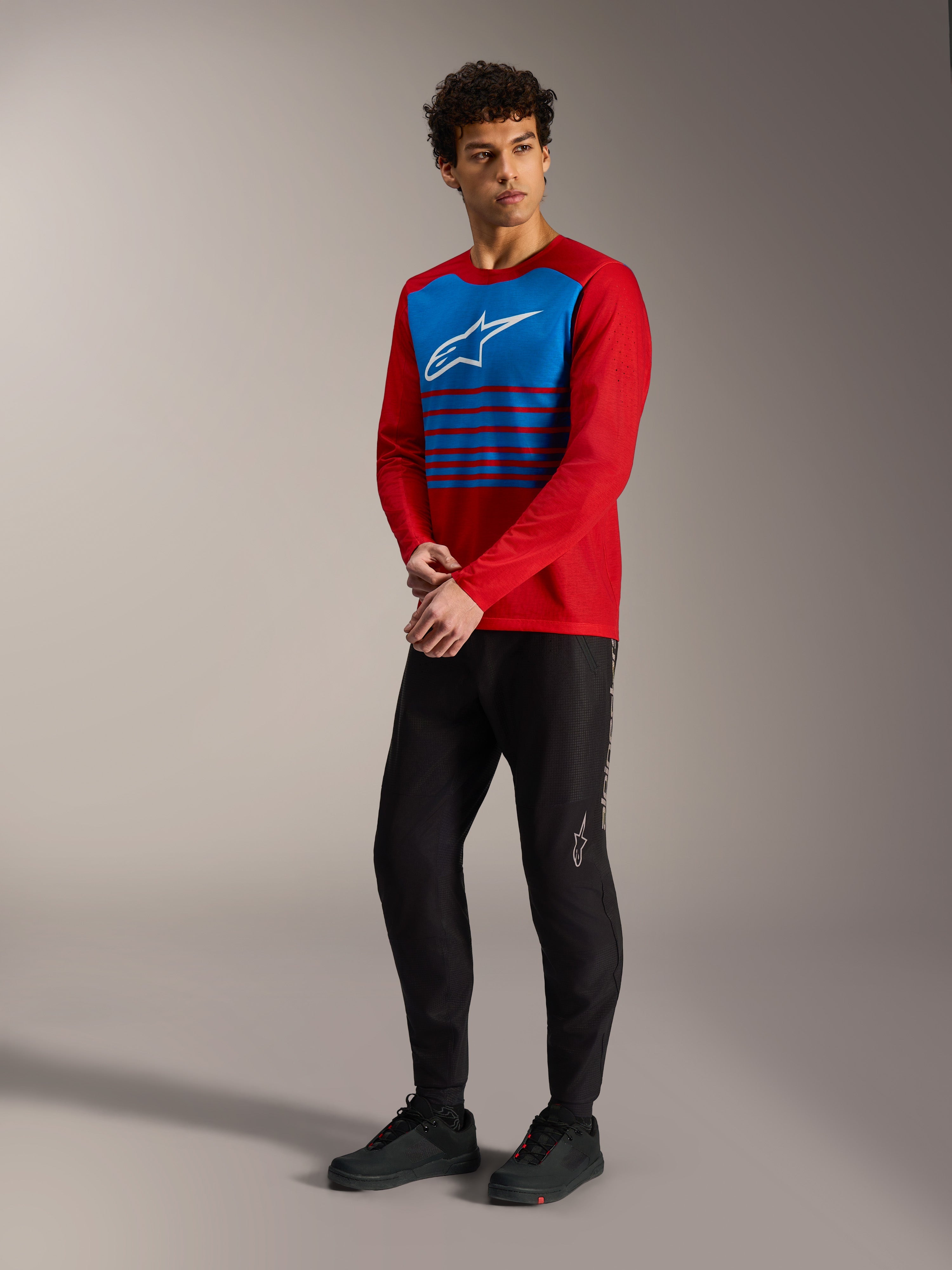 Jersey A-Dura Elite 2.0 rojo con panel de rayas azules en el pecho, logo blanco y pantalones MTB negros.