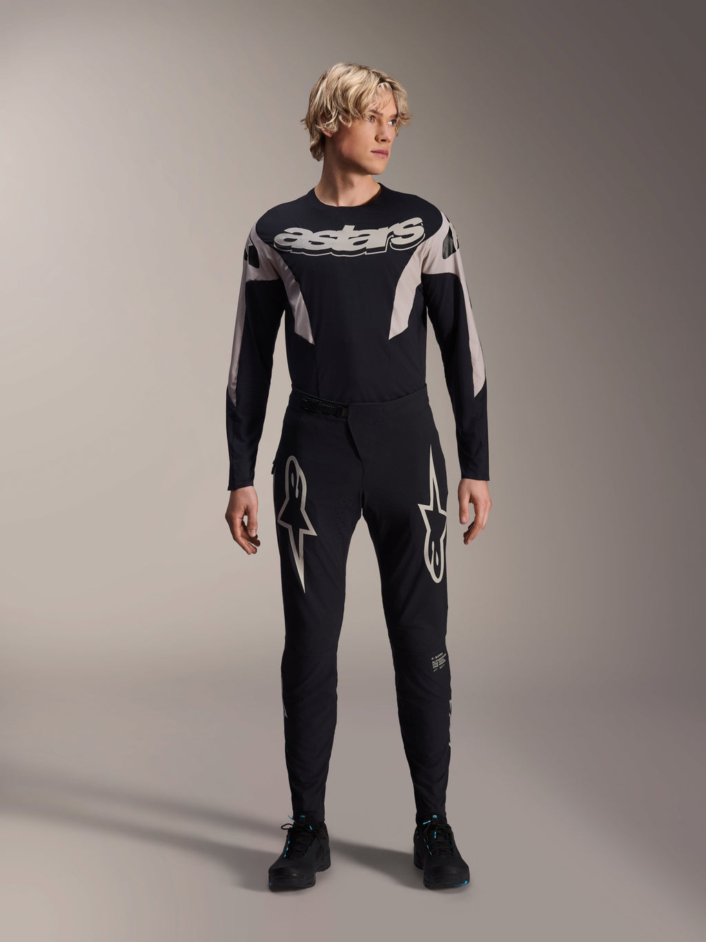 Pantalones Alpinestars A-Supra Melt y jersey de manga larga a juego, modelo con equipación negra de MTB con grandes gráficos de estrellas blancas en los muslos y marca 'astars' en el pecho, ropa profesional para carreras de bicicleta de montaña.