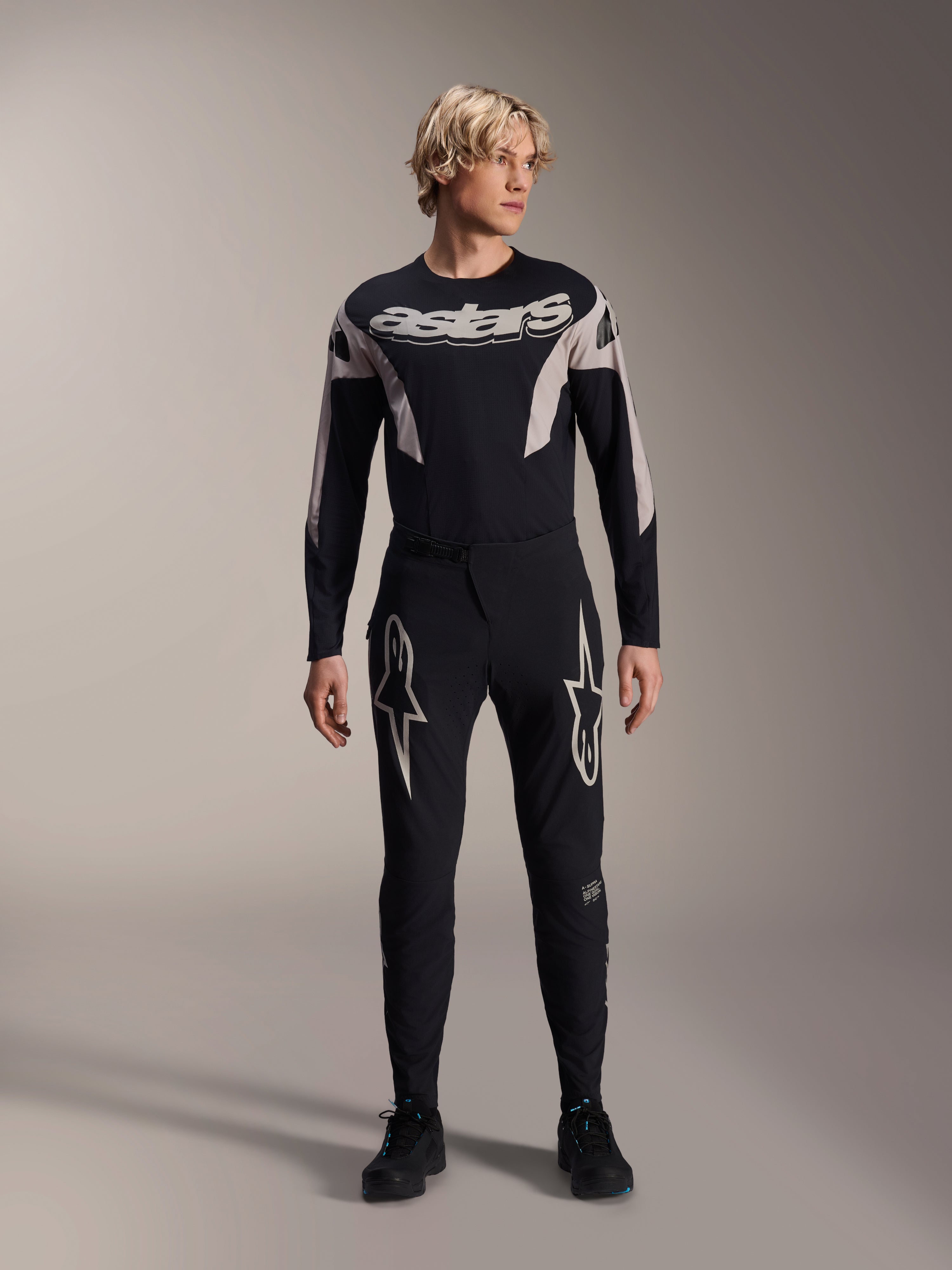 Pantalones Alpinestars A-Supra Melt y jersey de manga larga a juego, modelo con equipación negra de MTB con grandes gráficos de estrellas blancas en los muslos y marca 'astars' en el pecho, ropa profesional para carreras de bicicleta de montaña.