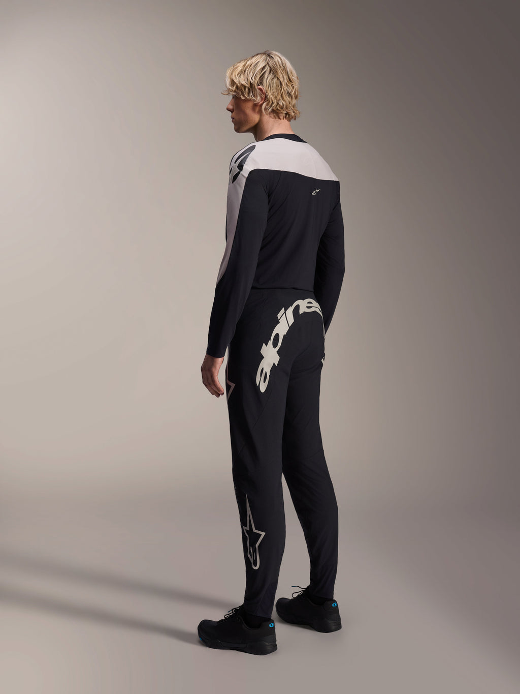 Jersey Alpinestars A-Supra Melt de manga larga, negro con paneles blancos en los hombros, visto desde atrás y de lado en un modelo, combinado con pantalones negros de MTB con un logotipo grande en blanco, equipamiento de carreras de alto rendimiento