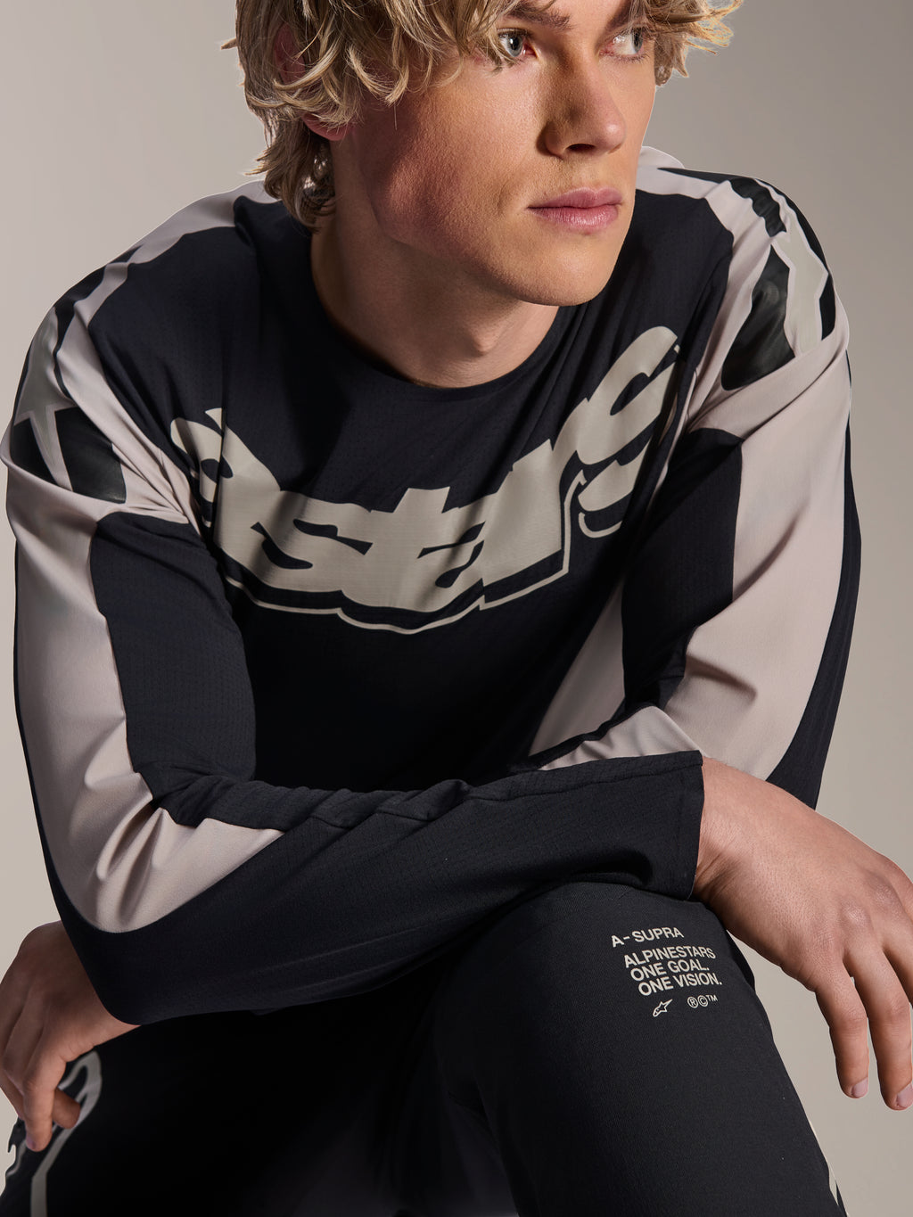 Jersey Alpinestars A-Supra Melt, jersey de MTB de manga larga, negro con gráficos en gris claro, usado por un modelo, con logotipo llamativo en el pecho y marca 'One Goal. One Vision.', ropa técnica de alto rendimiento para ciclismo de montaña