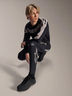 Pantalones y jersey de manga larga Alpinestars A-Supra Melt, negro y gris, con logotipos de estrella y marca destacados en blanco, lucidos por un modelo masculino en una pose agachada, equipamiento coordinado de carreras MTB
