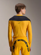 Alpinestars Limited Edition A-Supra Melt Gold Gear-Set, Yellow MTB Gear Set, back view of model wearing long-sleeve jersey with black shoulder panel and matching yellow pants featuring a large black logo on the rear, high-performance cycling apparel.