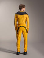 Rear view of a model wearing the Alpinestars Limited Edition A-Supra Melt Gold Gear-Set, featuring a dark yellow long-sleeve jersey with a black shoulder yoke and matching dark yellow pants with a large black Alpinestars wordmark across the back yoke, paired with black shoes.