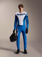 Modelo masculino con el kit de MTB Alpinestars A-Supra Melt, jersey de manga larga blanco y azul con la inscripción "astars", pantalones azules A-Supra Melt con logo blanco, casco integral negro, guantes y zapatillas negros, conjunto de ciclismo coordinado para todoterreno