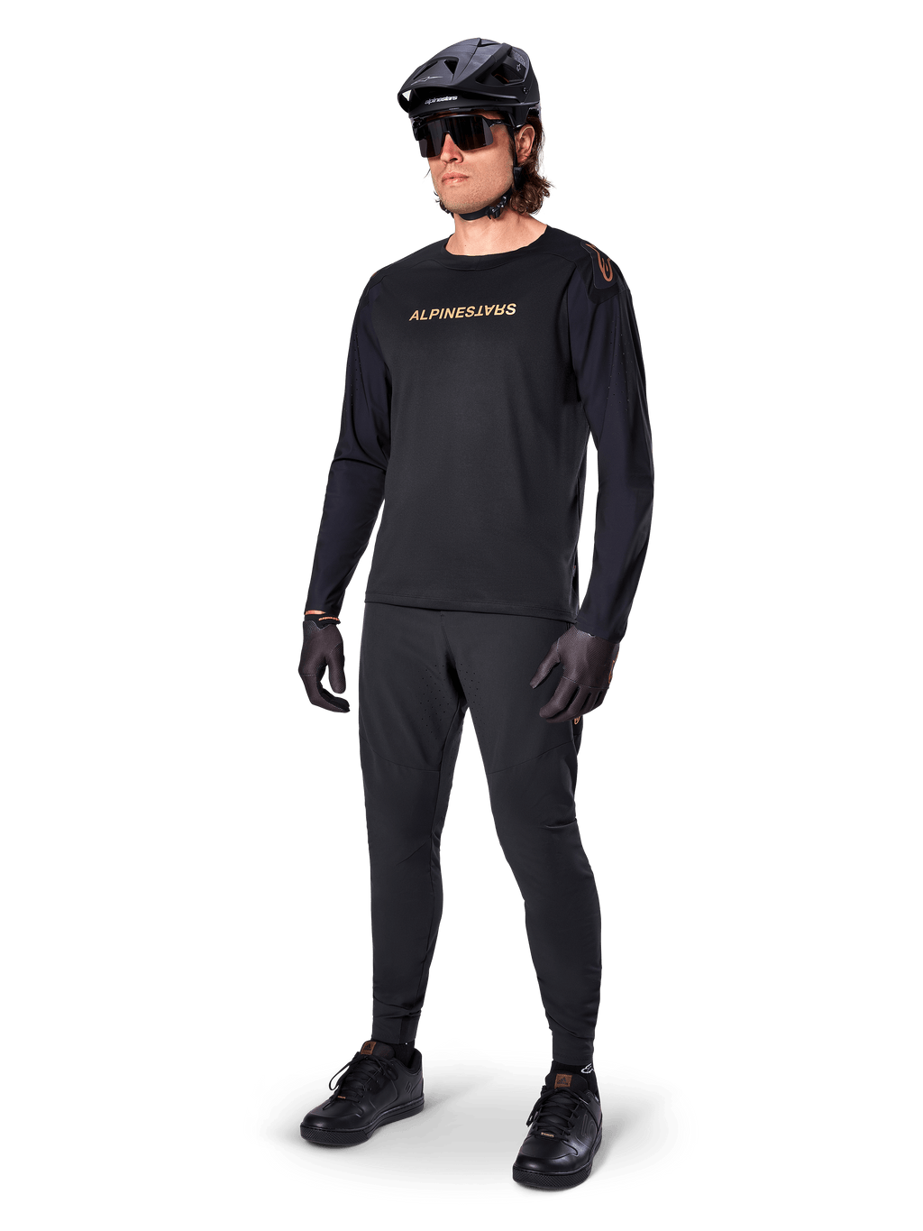 Jersey Alpinestars A-Aria Polartec Switch de manga larga, negro, logotipo en bronce en el pecho, usado por un ciclista de montaña con casco negro y gafas de sol, ropa de ciclismo de alto rendimiento para trail