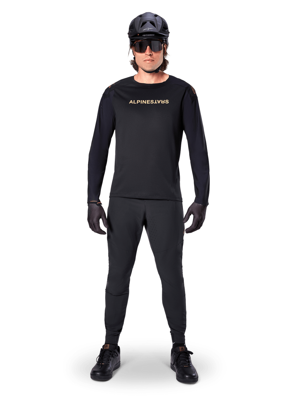 Alpinestars Jersey de manga larga A-Aria Polartec Switch, negro, usado por un ciclista con pantalones técnicos negros a juego, casco negro, gafas de sol y guantes negros, equipamiento de MTB de alto rendimiento para senderos todoterreno