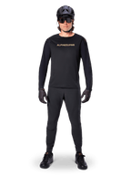 Alpinestars Jersey de manga larga A-Aria Polartec Switch, negro, usado por un ciclista con pantalones técnicos negros a juego, casco negro, gafas de sol y guantes negros, equipamiento de MTB de alto rendimiento para senderos todoterreno