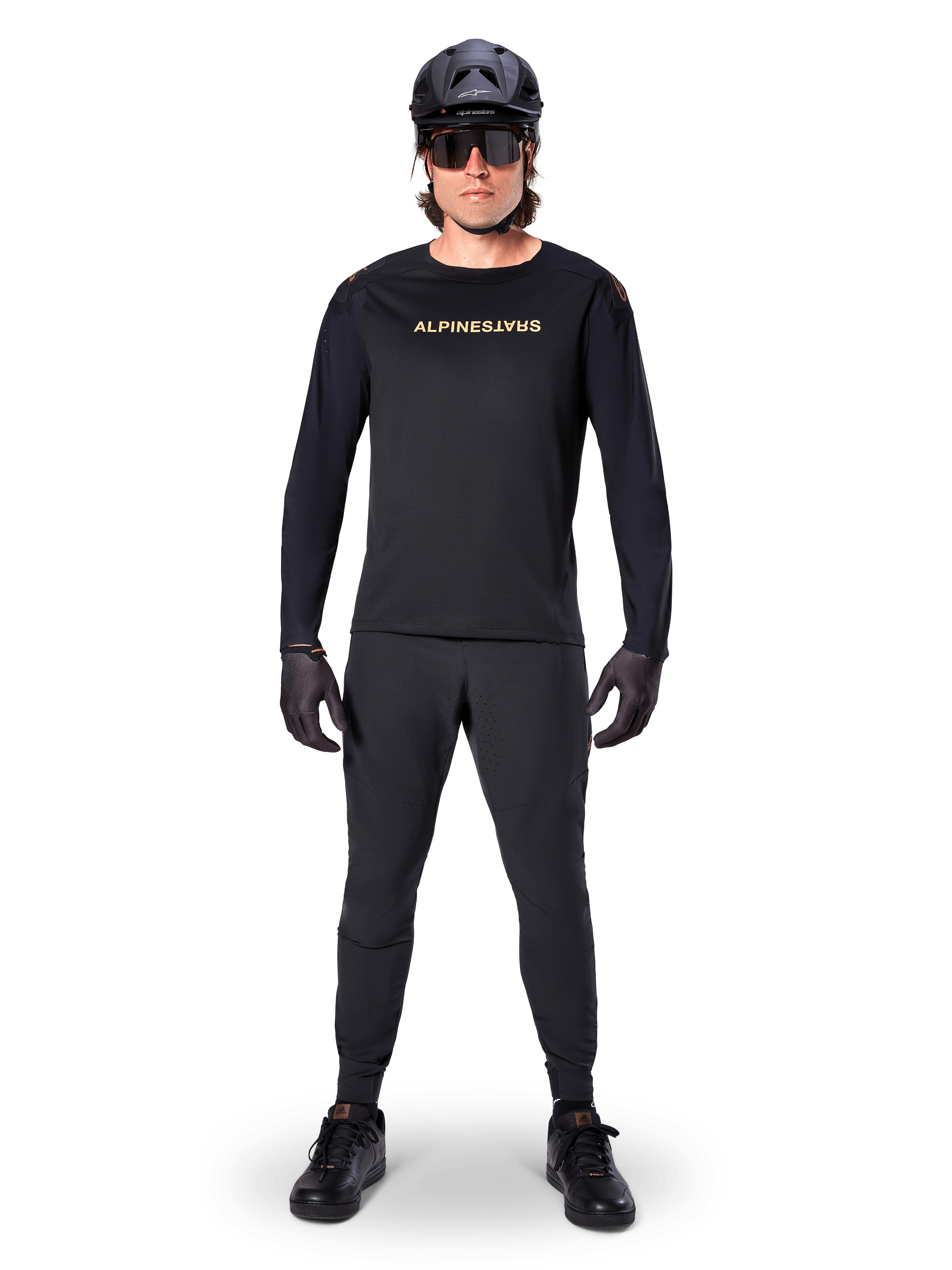 Alpinestars Jersey de manga larga A-Aria Polartec Switch, negro, usado por un ciclista con pantalones técnicos negros a juego, casco negro, gafas de sol y guantes negros, equipamiento de MTB de alto rendimiento para senderos todoterreno