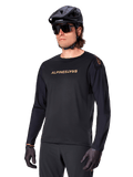Alpinestars Jersey de manga larga A-Aria Polartec Switch, negro con logotipo dorado, ropa de ciclismo de montaña MTB, usado con casco negro y gafas de sol, con ventilación cortada con láser en las mangas y tejido Polartec que absorbe la humedad para un rendimiento off-road