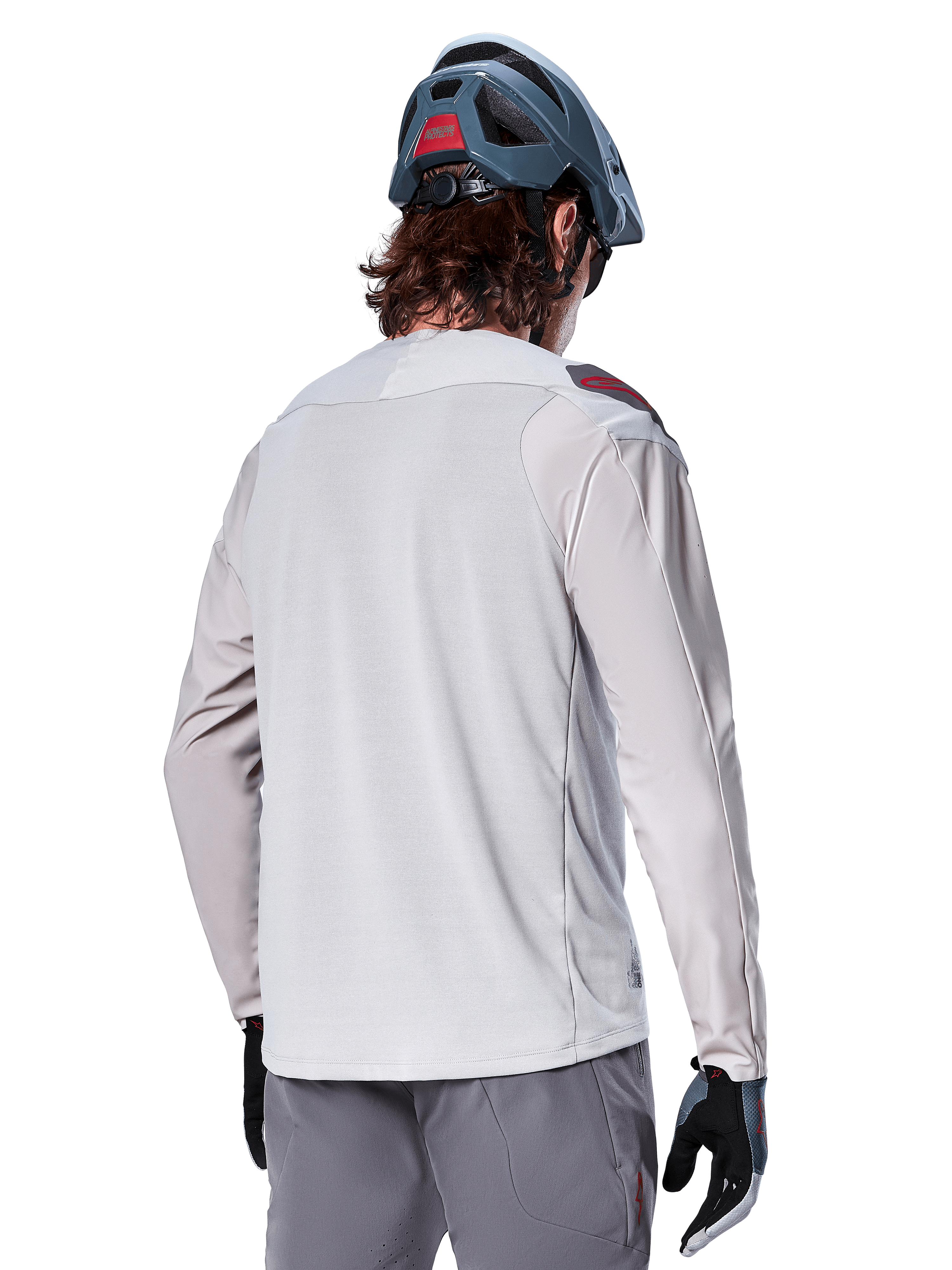 Jersey de manga larga Alpinestars A-Aria Polartec Switch, gris claro, visto desde atrás en un ciclista, usado con un casco de montaña azul y pantalones grises, ropa de rendimiento para ciclismo de montaña en senderos todoterreno