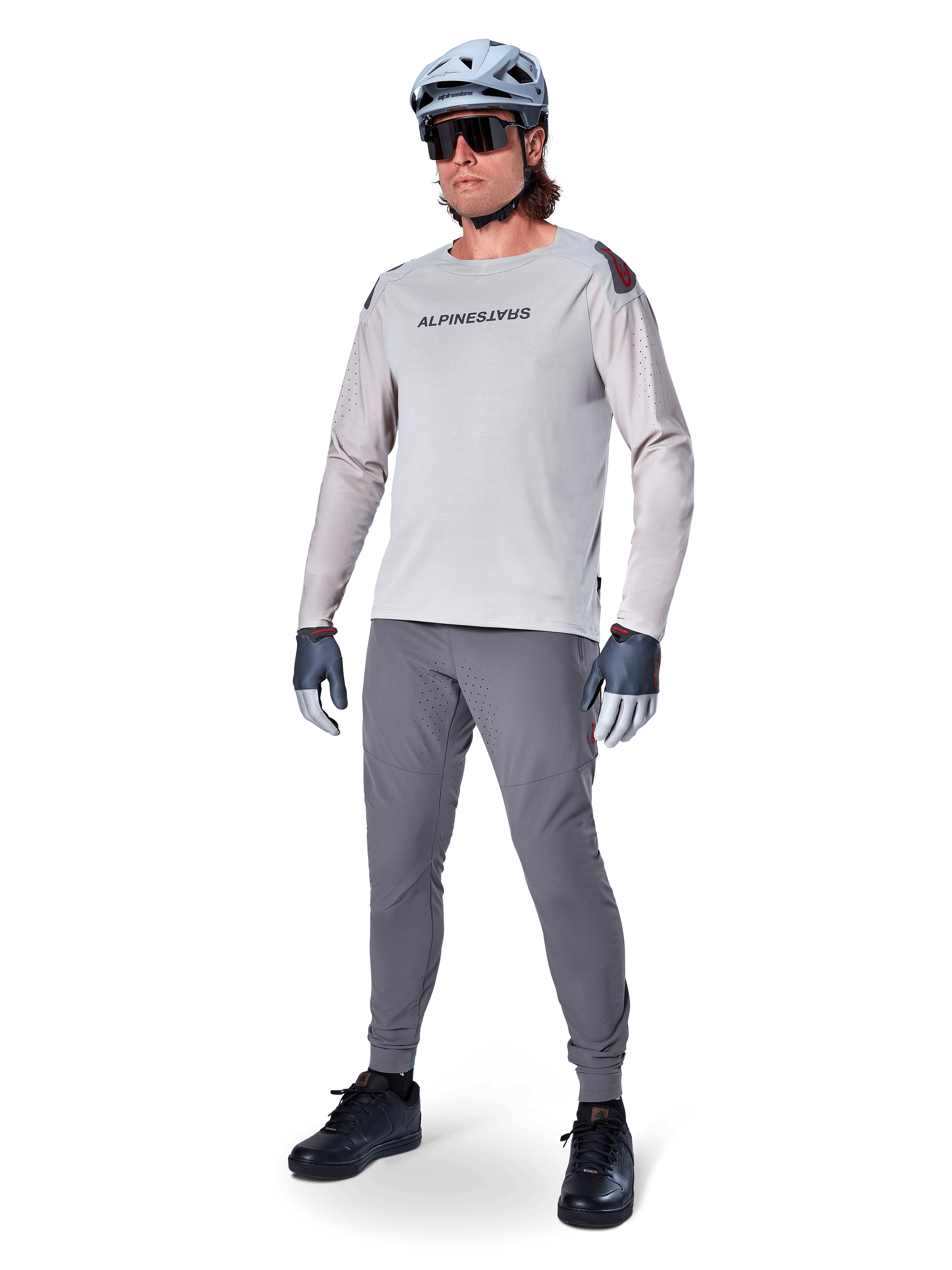 Alpinestars A-Aria Polartec Switch Jersey, jersey de MTB de manga larga, gris claro, usado con pantalones de MTB gris oscuro, casco y guantes, con mangas perforadas con láser y logotipo de Alpinestars en el pecho.