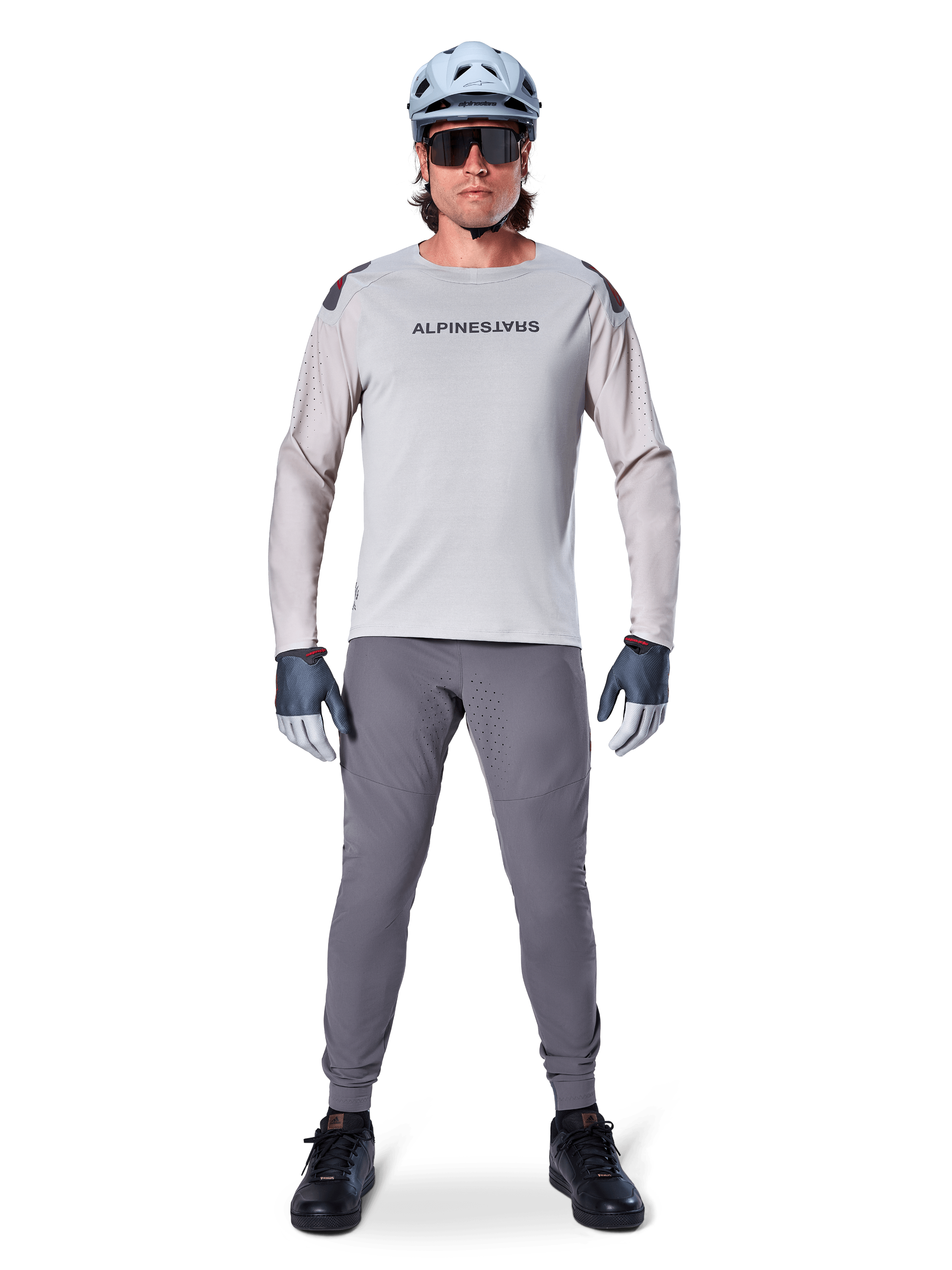Jersey Alpinestars A-Aria Polartec Switch de manga larga, gris claro, usado por un ciclista de montaña con pantalones de MTB gris oscuro, casco azul claro y gafas de sol, con logotipo en el pecho y ventilación perforada por láser en las mangas, equipamiento completo para ciclismo todoterreno