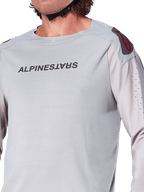 Primer plano del jersey de manga larga Alpinestars A-Aria Polartec Switch en gris claro, con logotipo de Alpinestars en el pecho, logo rojo en el hombro y mangas con perforaciones láser para el flujo de aire, equipamiento premium para ciclismo de montaña