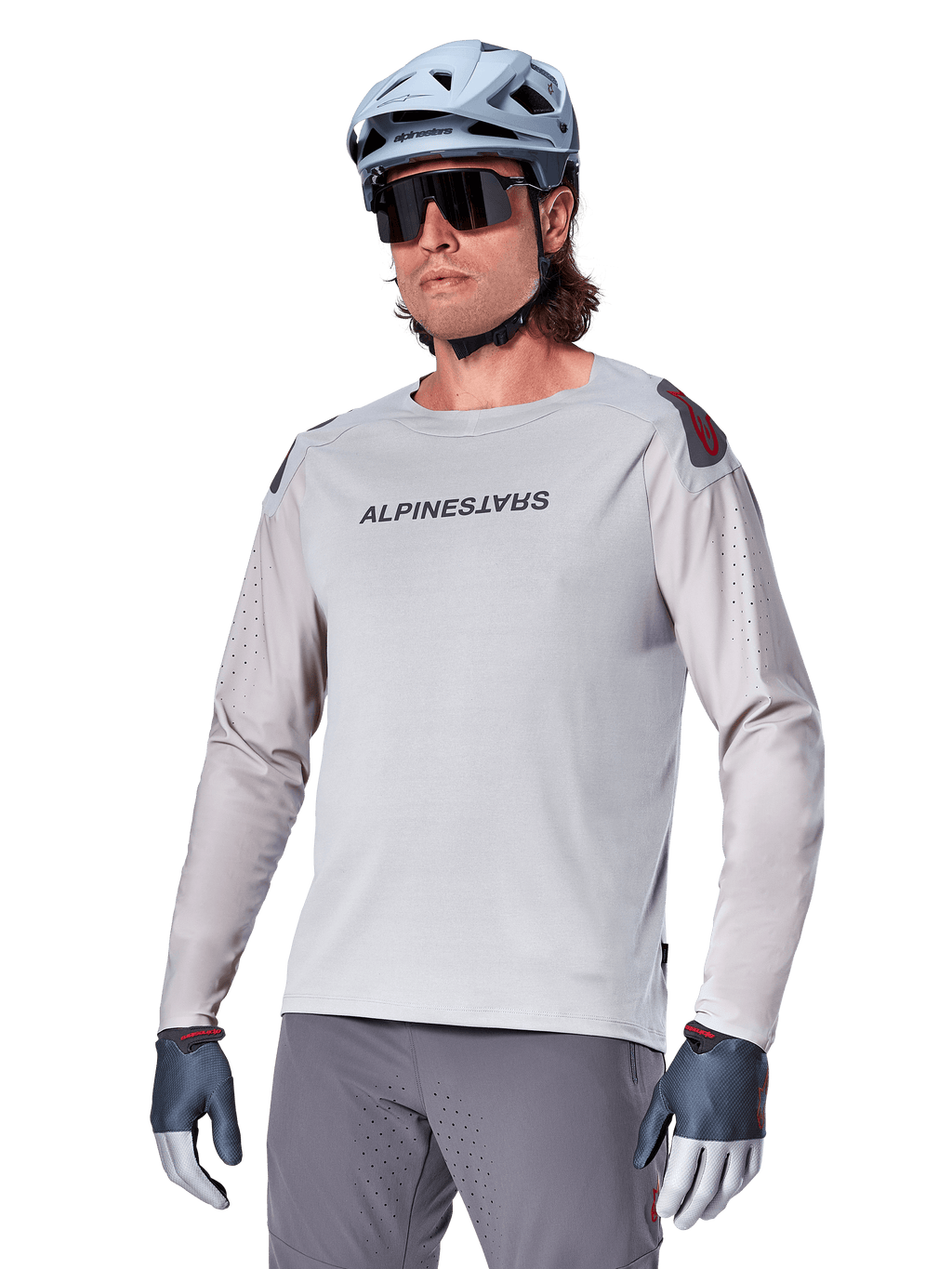 Alpinestars A-Aria Polartec Switch Jersey de manga larga, camiseta de ciclismo gris claro con logotipo negro en el pecho y detalles rojos en los hombros, mangas perforadas con láser para ventilación, combinada con casco azul claro, gafas de sol y pantalones grises, ropa técnica de montaña para trail