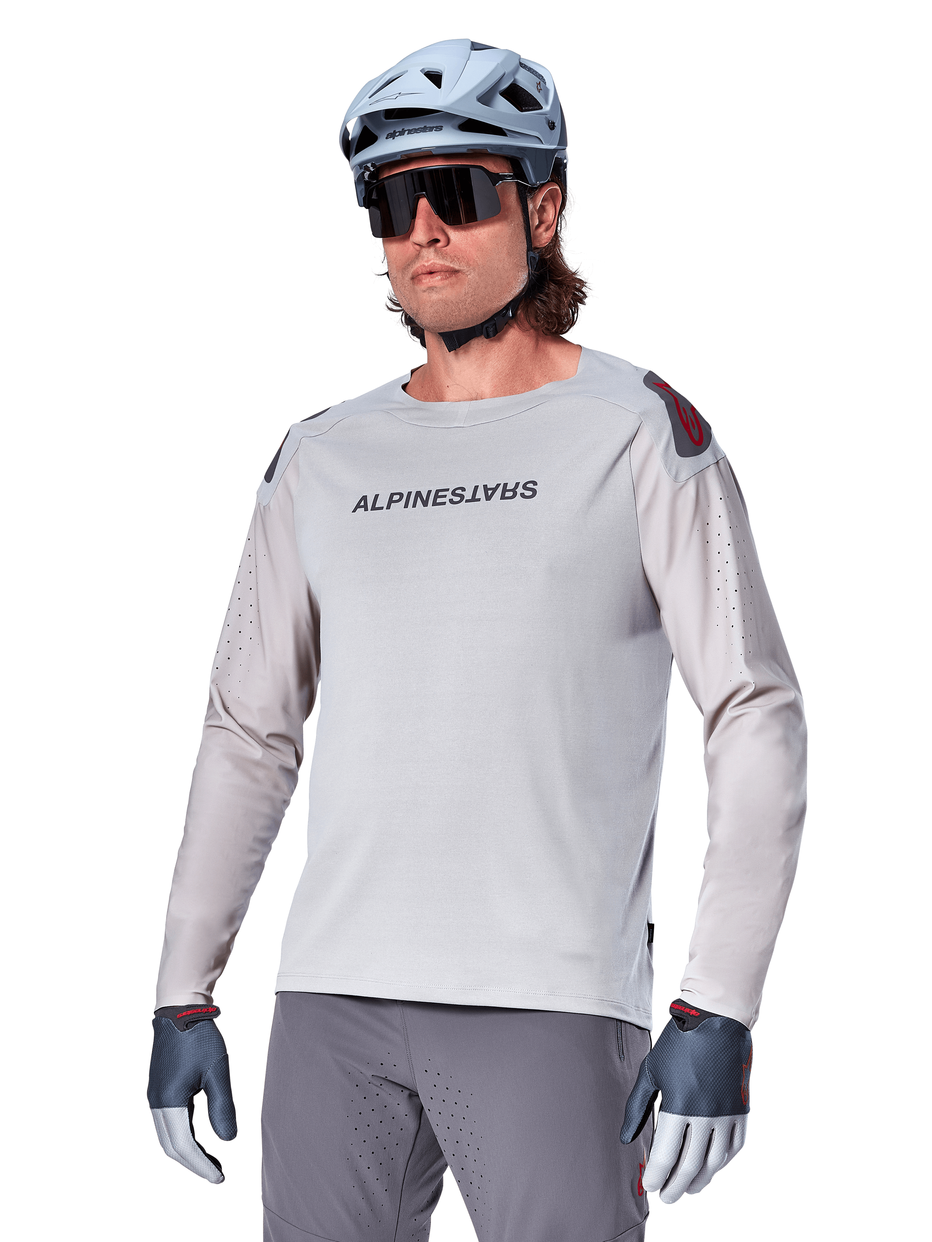 Alpinestars A-Aria Polartec Switch Jersey de manga larga, camiseta de ciclismo gris claro con logotipo negro en el pecho y detalles rojos en los hombros, mangas perforadas con láser para ventilación, combinada con casco azul claro, gafas de sol y pantalones grises, ropa técnica de montaña para trail