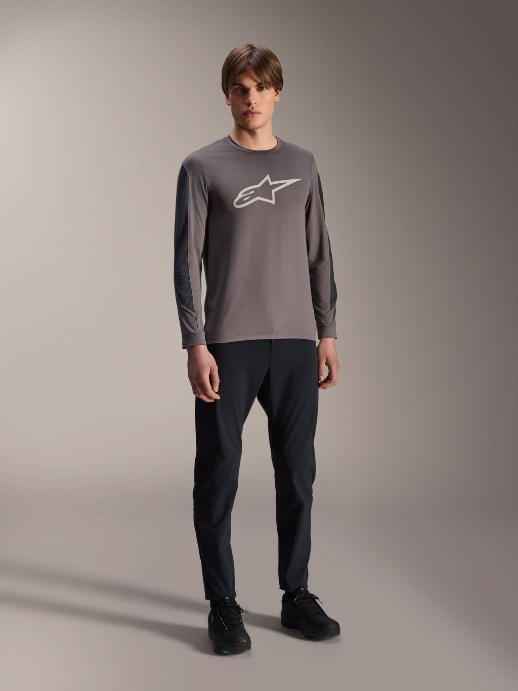 Jersey Alpinestars A-Dura Insert Astar, jersey de MTB de manga larga, gris oscuro, con un gran logotipo blanco en el pecho, usado con pantalones técnicos negros y calzado negro, ropa de ciclismo todoterreno