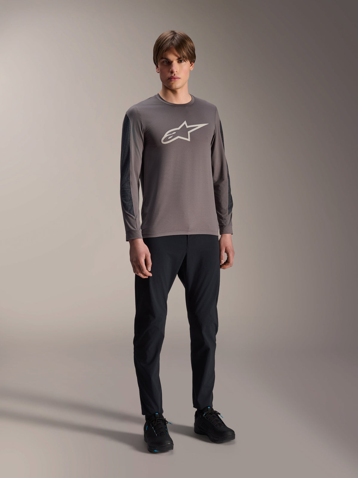 Jersey Alpinestars A-Dura Insert Astar, jersey de MTB de manga larga, gris oscuro, con un gran logotipo blanco en el pecho, usado con pantalones técnicos negros y calzado negro, ropa de ciclismo todoterreno