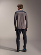 Alpinestars A-Dura Insert Astar Long Sleeve Jersey en gris oscuro, vista trasera, con paneles de color carbón en los hombros y una etiqueta roja en el dobladillo, combinado con pantalones y calzado negros, ropa técnica para bicicleta de montaña