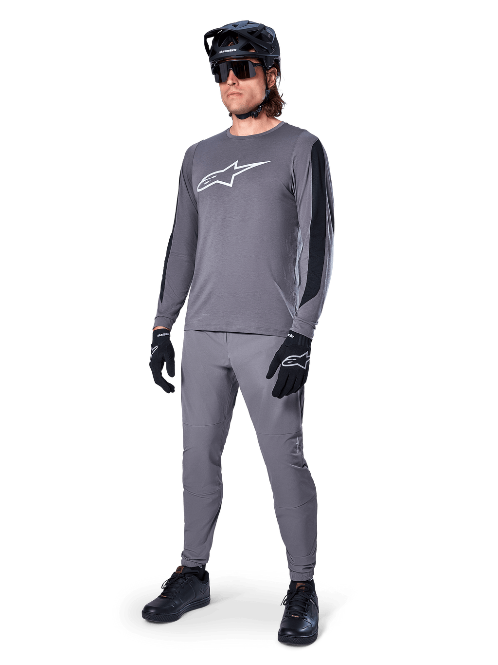 Jersey Alpinestars A-Dura Dri Astar, jersey de MTB de manga larga, gris oscuro con logo blanco en el pecho, paneles de malla negros en las mangas, usado con pantalones grises a juego, casco negro y guantes, equipamiento de alto rendimiento para bicicleta de montaña