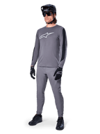 Jersey Alpinestars A-Dura Dri Astar, jersey de MTB de manga larga, gris oscuro con logo blanco en el pecho, paneles de malla negros en las mangas, usado con pantalones grises a juego, casco negro y guantes, equipamiento de alto rendimiento para bicicleta de montaña