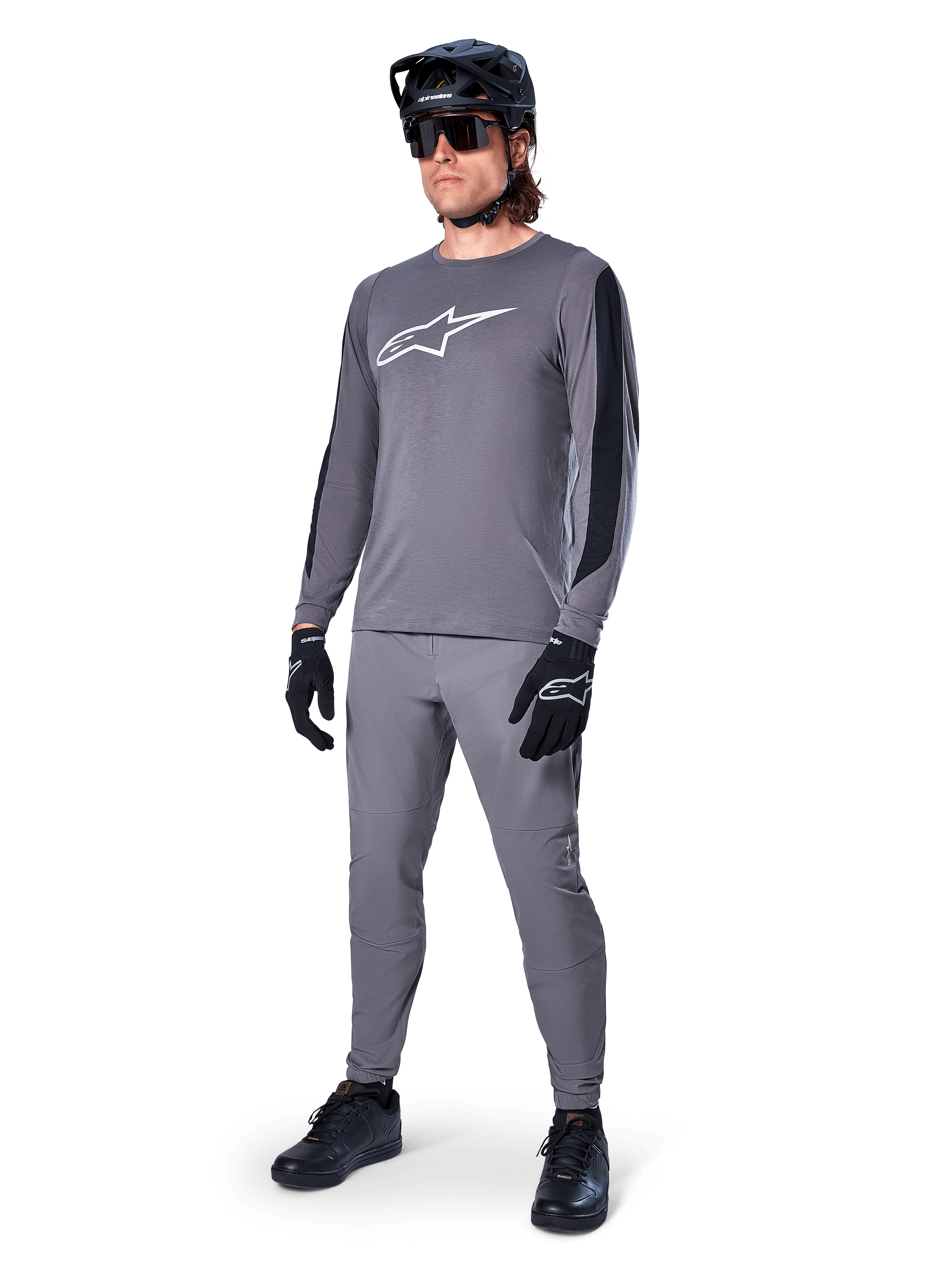 Jersey Alpinestars A-Dura Dri Astar, jersey de MTB de manga larga, gris oscuro con logo blanco en el pecho, paneles de malla negros en las mangas, usado con pantalones grises a juego, casco negro y guantes, equipamiento de alto rendimiento para bicicleta de montaña