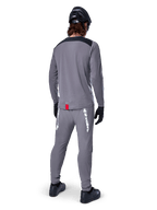 Jersey de manga larga Alpinestars A-Dura Dri Astar, gris oscuro, vista posterior del ciclista con pantalones a juego y casco negro, cuenta con paneles negros en los hombros y una pequeña etiqueta roja en el dobladillo, equipamiento técnico para ciclismo todoterreno