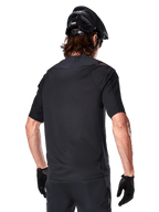 Jersey Alpinestars A-Aria Polartec Switch de manga corta, negro, vista trasera en un ciclista con casco de montaña negro, pantalones cortos y guantes negros a juego, equipamiento de alto rendimiento para ciclismo de montaña