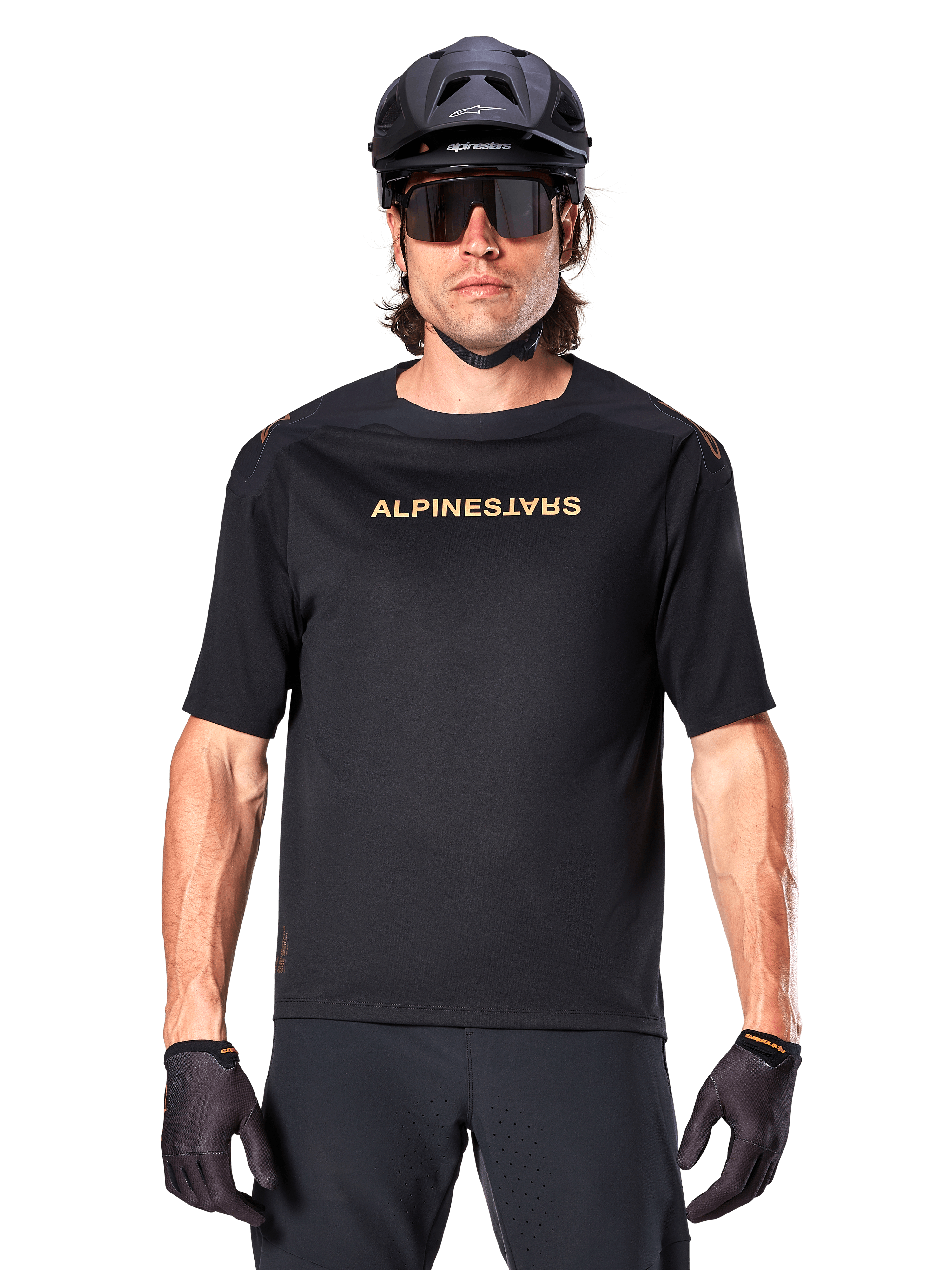 Ciclista de montaña con el jersey Alpinestars A-Aria Polartec Switch de manga corta en color negro, con logotipo dorado en el pecho, combinado con casco de MTB negro, gafas de sol oscuras de alto rendimiento y guantes a juego, equipamiento de ciclismo de montaña.