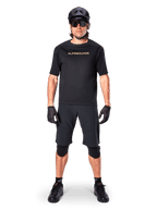 Alpinestars A-Aria Polartec Switch Jersey, jersey de MTB de manga corta, negro con letras en color canela, usado con equipamiento de mountain bike negro coordinado que incluye casco, pantalones cortos y rodilleras, ropa de ciclismo de alto rendimiento para off-road
