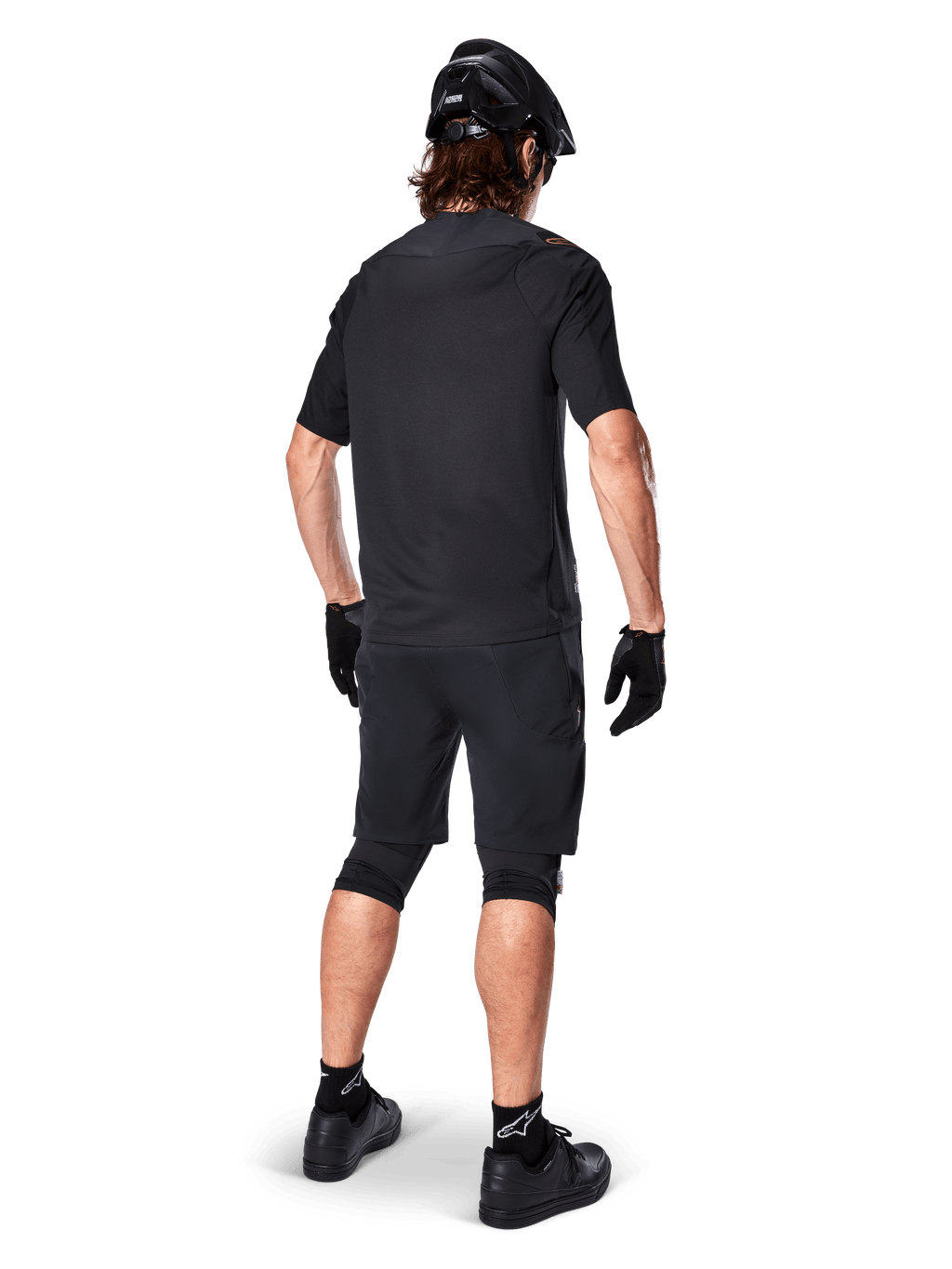 Ciclista de montaña masculino visto desde atrás con el Jersey Alpinestars A-Aria Polartec Switch en color negro, camiseta de MTB de manga corta, combinada con pantalones cortos de montaña negros, casco y guantes negros, equipación técnica de alto rendimiento para rutas de senderos