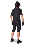 Ciclista de montaña masculino visto desde atrás con el Jersey Alpinestars A-Aria Polartec Switch en color negro, camiseta de MTB de manga corta, combinada con pantalones cortos de montaña negros, casco y guantes negros, equipación técnica de alto rendimiento para rutas de senderos