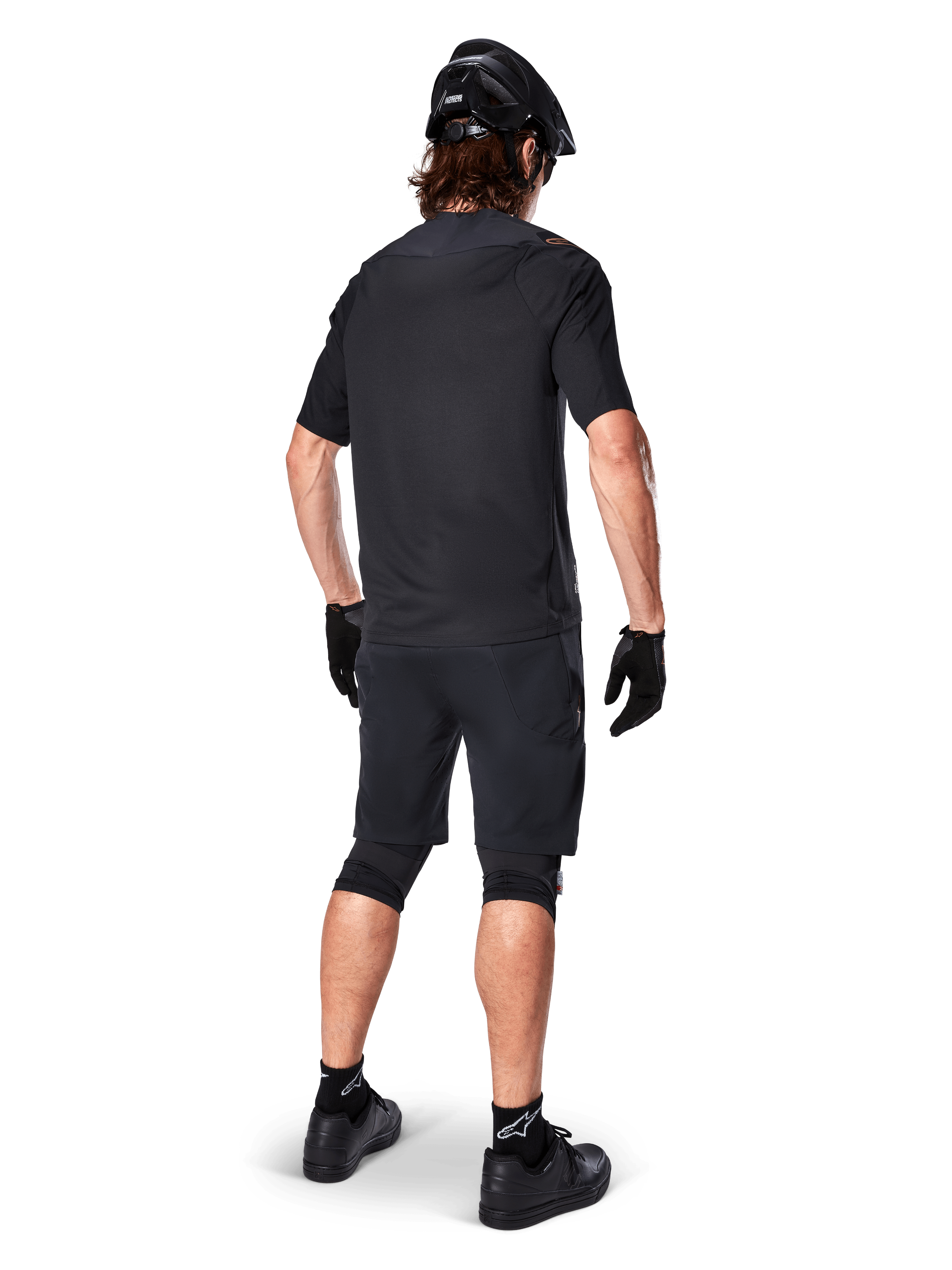 Ciclista de montaña masculino visto desde atrás con el Jersey Alpinestars A-Aria Polartec Switch en color negro, camiseta de MTB de manga corta, combinada con pantalones cortos de montaña negros, casco y guantes negros, equipación técnica de alto rendimiento para rutas de senderos