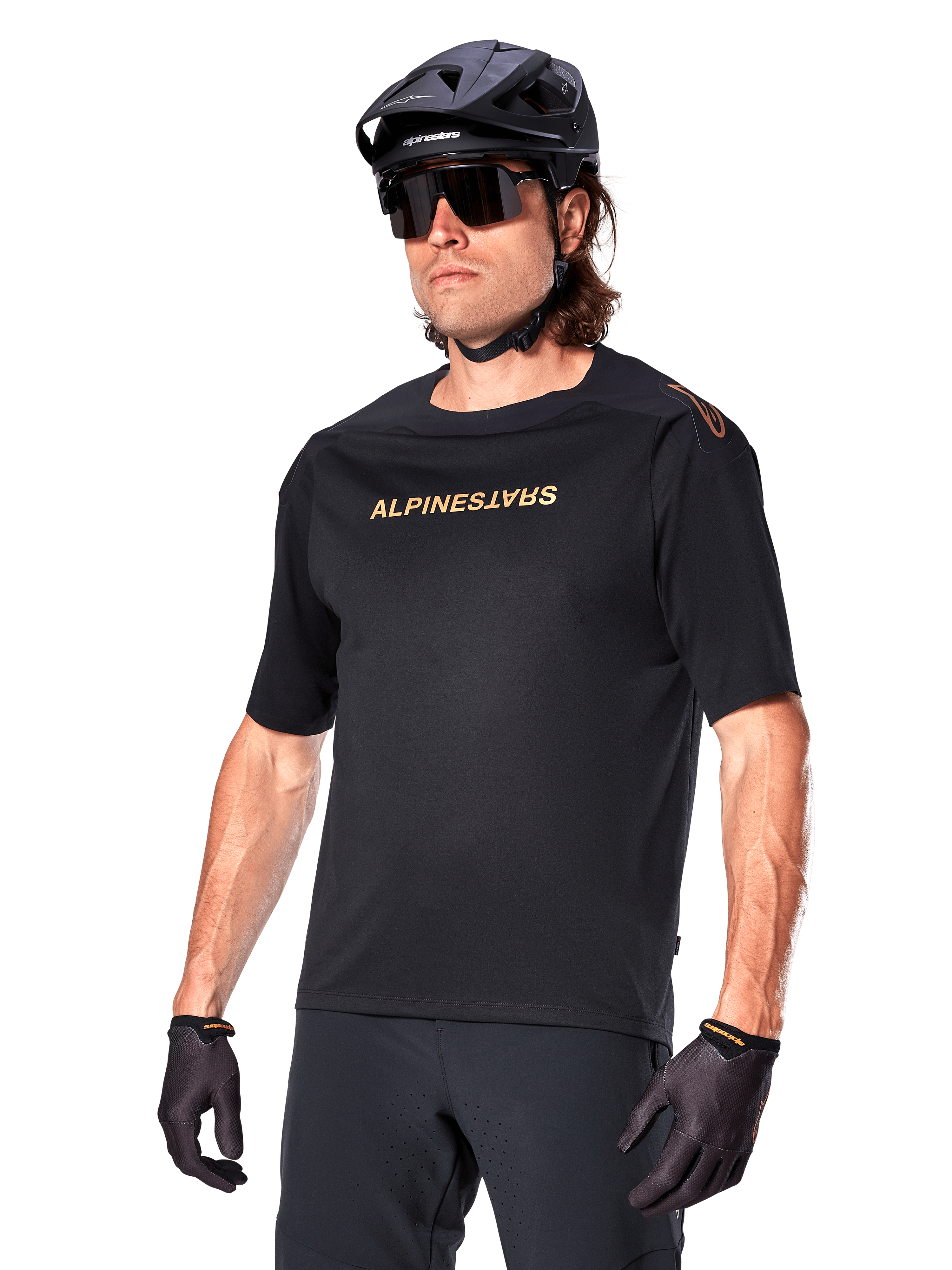 Alpinestars A-Aria Polartec Switch Jersey de manga corta, camiseta negra de ciclismo de montaña con la marca Alpinestars en dorado, usada con casco negro, gafas de sol y guantes, equipamiento técnico de MTB