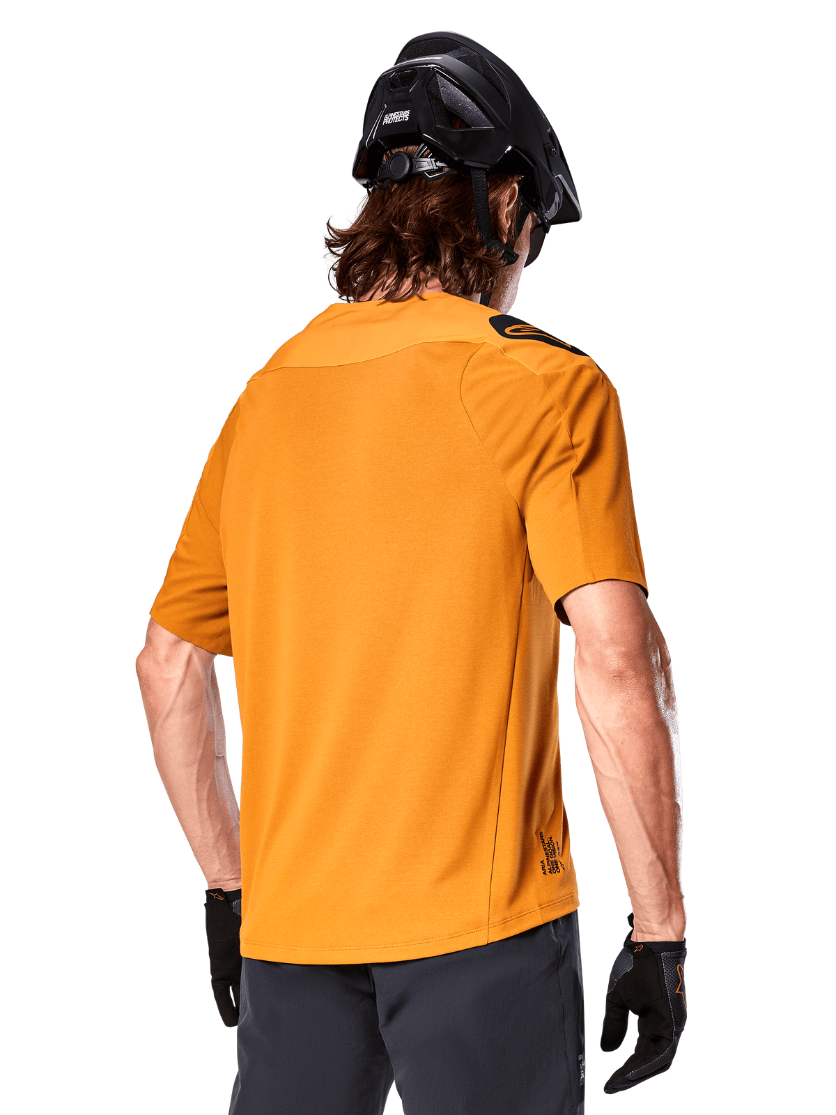 Jersey Alpinestars A-Aria Polartec Switch, camiseta de MTB de manga corta, color oro oscuro, vista posterior que muestra el ajuste de rendimiento, usado con casco negro y pantalones cortos grises, ropa de trail duradera y transpirable
