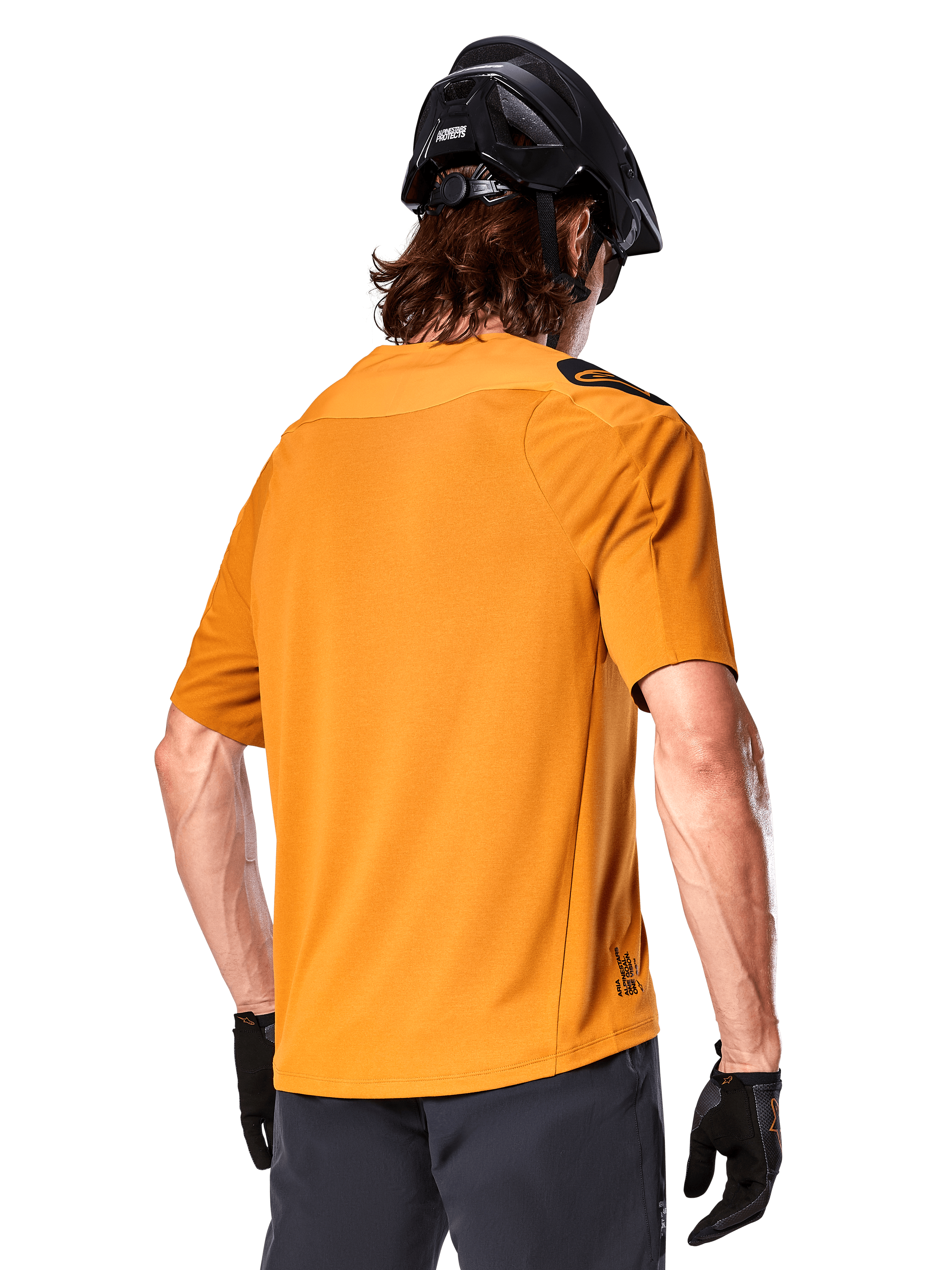 Jersey Alpinestars A-Aria Polartec Switch, camiseta de MTB de manga corta, color oro oscuro, vista posterior que muestra el ajuste de rendimiento, usado con casco negro y pantalones cortos grises, ropa de trail duradera y transpirable